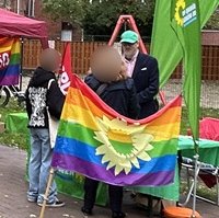 Ein Mitglied des Grünen Ortsverbands Norden-Krummhörm am Stand bei der Herbst Pride Norden 2025 mit Grünen Beachflags und Regenbogenflagge