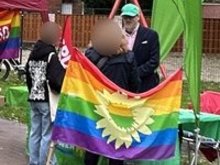 Ein Mitglied des Grünen Ortsverbands Norden-Krummhörm am Stand bei der Herbst Pride Norden 2025 mit Grünen Beachflags und Regenbogenflagge